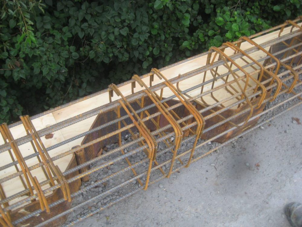 Stahlbewehrung aus Längsstäben und Bügeln entlang einer Holzschalung am Rand einer Betonfläche.