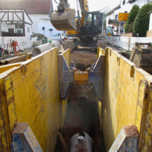 Blick in einen tiefen Rohrgraben, dessen Wände mit gelben Stahlplatten und Querstreben abgestützt sind.
