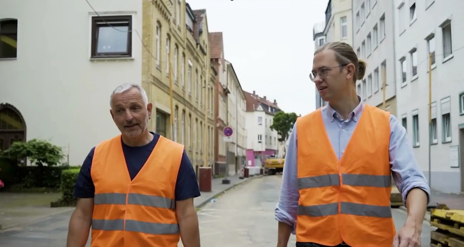 zwei Mitarbeiter der Firma in Warnwesten gehen durch eine Straße