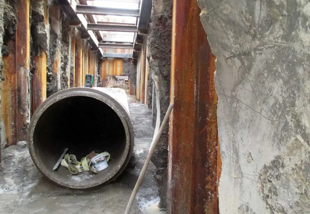 Großes Betonrohr in einem mit Stahlträgern abgestützten Baugraben