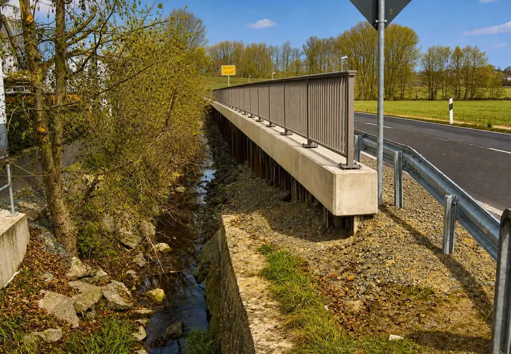 Neue Straßenbrücke mit Geländer über einem kleinen Bach